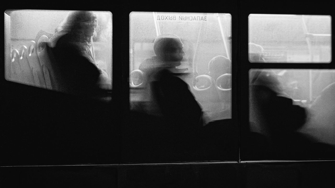 A black-and-white photograph of people riding on a bus taken through the window.