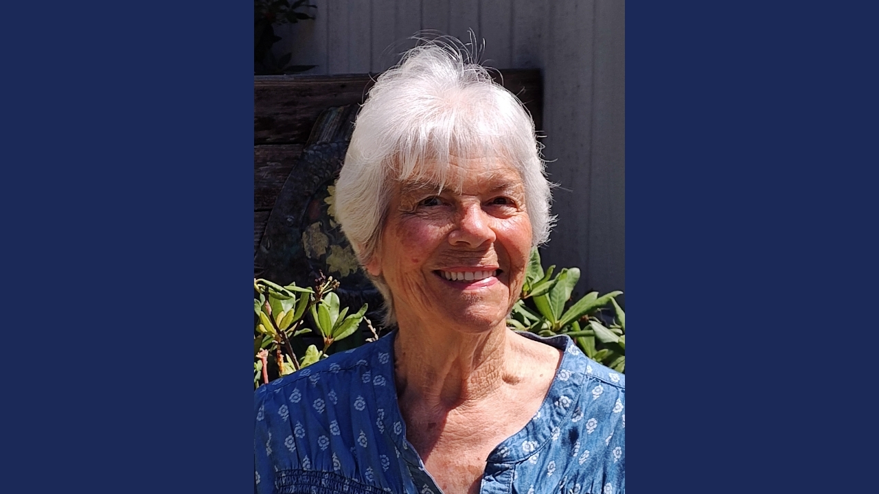 A photo of Ardean Maxey, an older woman with white hair standing outside in the sun and smiling.