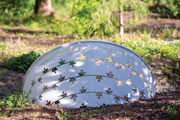 A metal sculpture in the form of a basket, half buried in earth