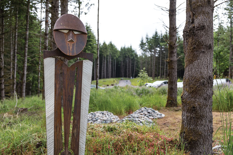 A metal and wood sculpture of a human figure installed amid woods