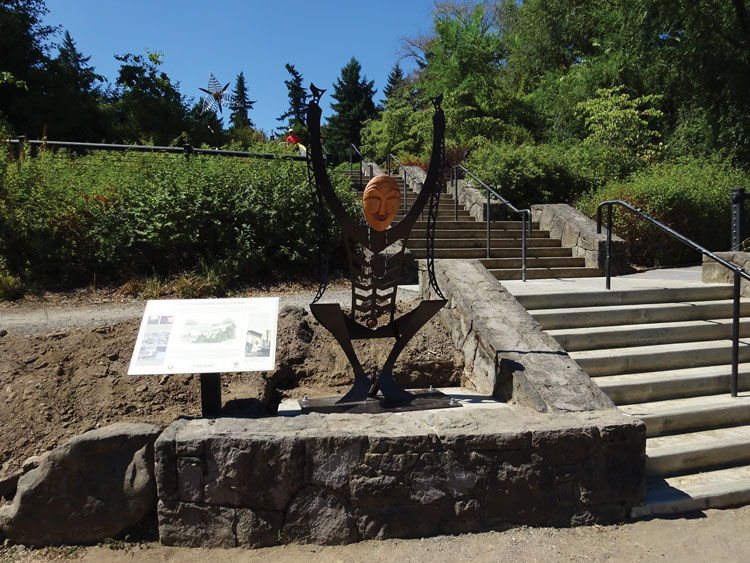 A metal and wood sculpture depicting a person raising their hands above their head